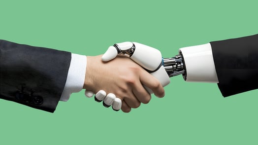 A man wearing a suit shakes hands with a robot wearing a suit. Only their arms are visible.