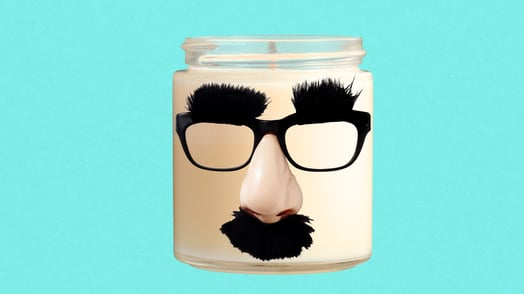 A white candle in a glass jar wearing fake glasses with an attached nose and mustache. 