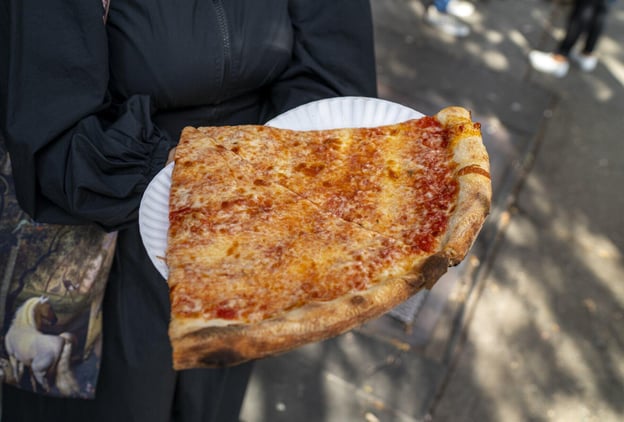 Person holding a large slice of NY style pizza on a paper plate