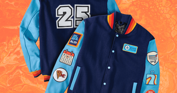 A blue Aldi-branded varsity jacket with the number 25 on it. Patches feature a calendar, Aldi's logo, a spice of pizza, and a shopping cart.