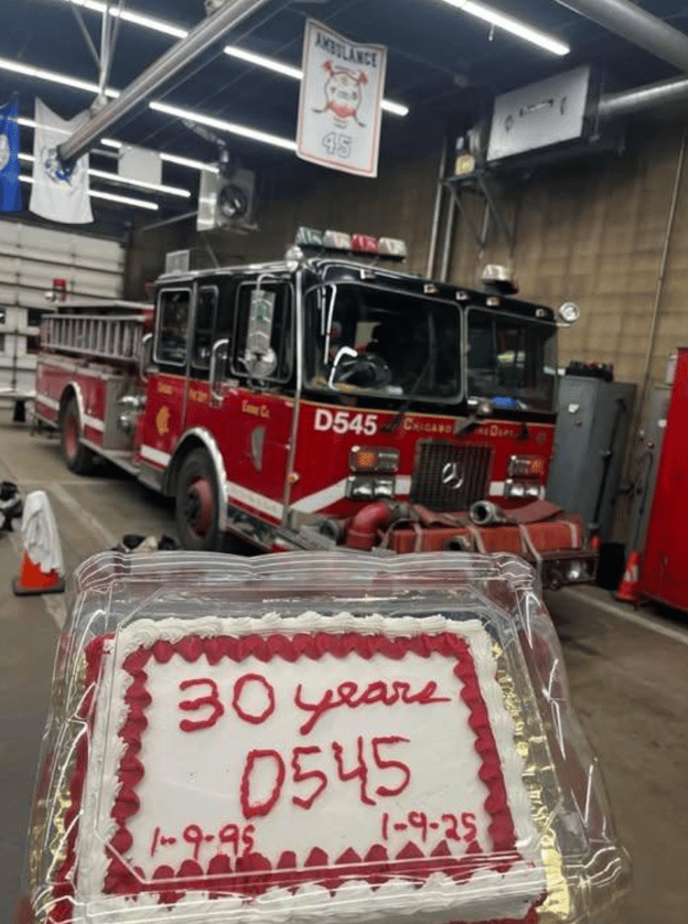 A white birthday cake with "30 years D545 1-9-95 1-9-25" in red icing sits in front of an aging red fire truck in a garage.