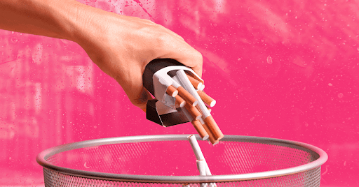 A hand emptying a pack of cigarettes into a trash can.